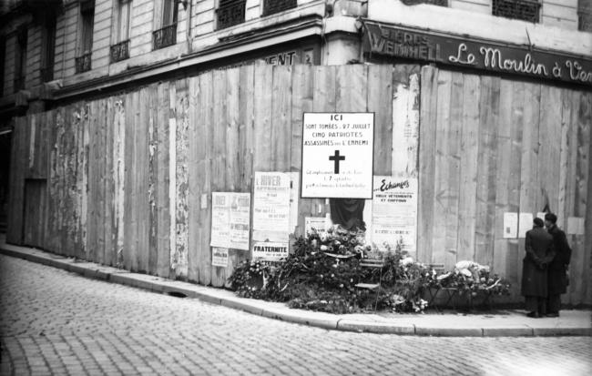 Libération de Lyon.  Lyon. Sur la palissade qui cache la devanture du café le "Moulin à vent", une grande affiche rappelle les 5 patriotes abattus par les Allemands à cet endroit. Mais d'autres affiches témoignent des difficultés persistantes du ravitaillement et de la reprise de la vie politique au grand jour.